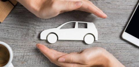 Hands protecting icon of car over wooden table. Top view of hands showing gesture of protecting car. Car insurance and automotive business concept.